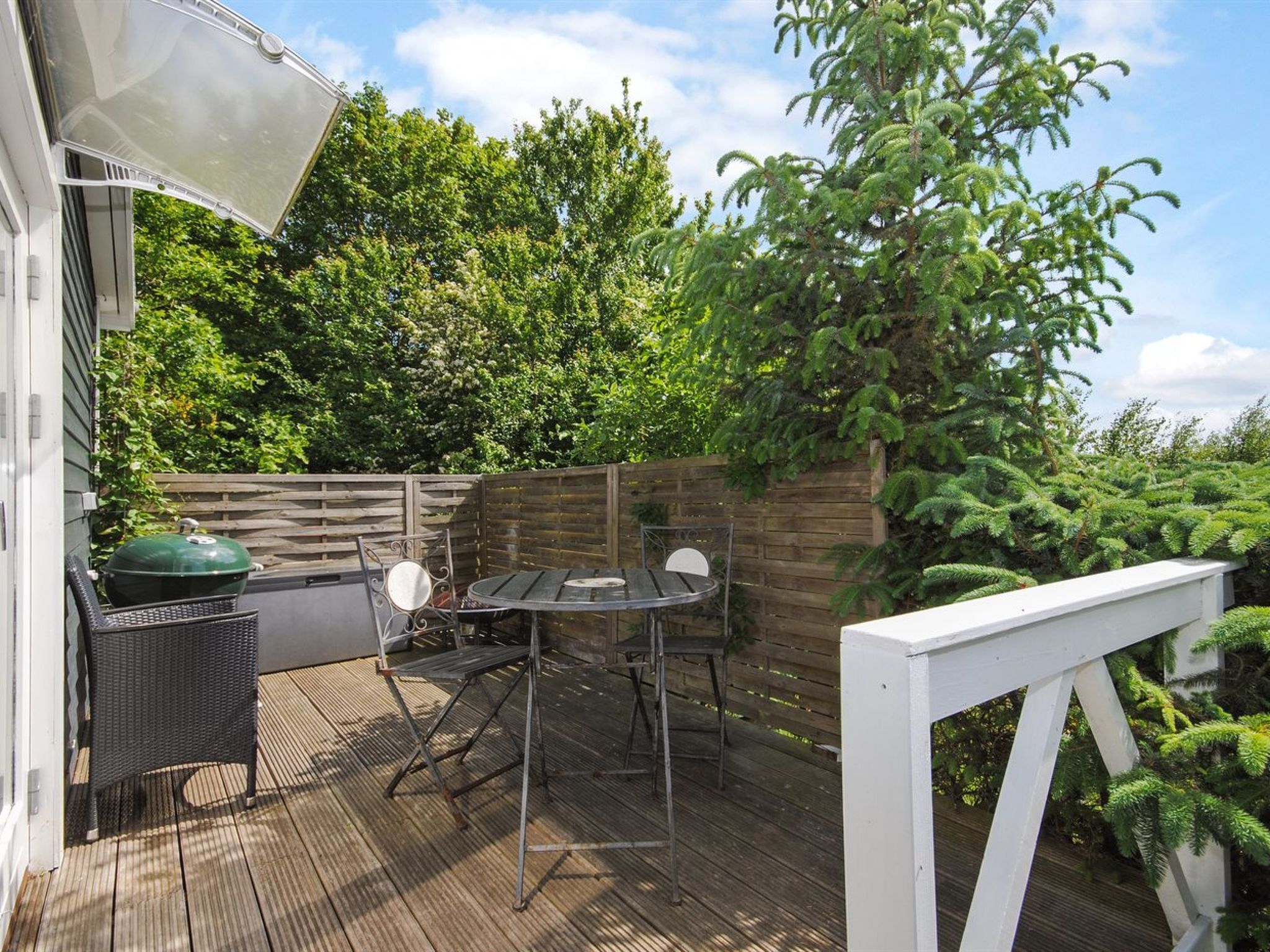 Une terrasse en bois avec une table et des chaises, un barbecue et une rambarde blanche.