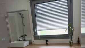 A modern bathroom with a large mirror, a sink, a shower, and a window with blinds. - 3 Bedroom Private vacation home in Blanquefort (Blanquefort)