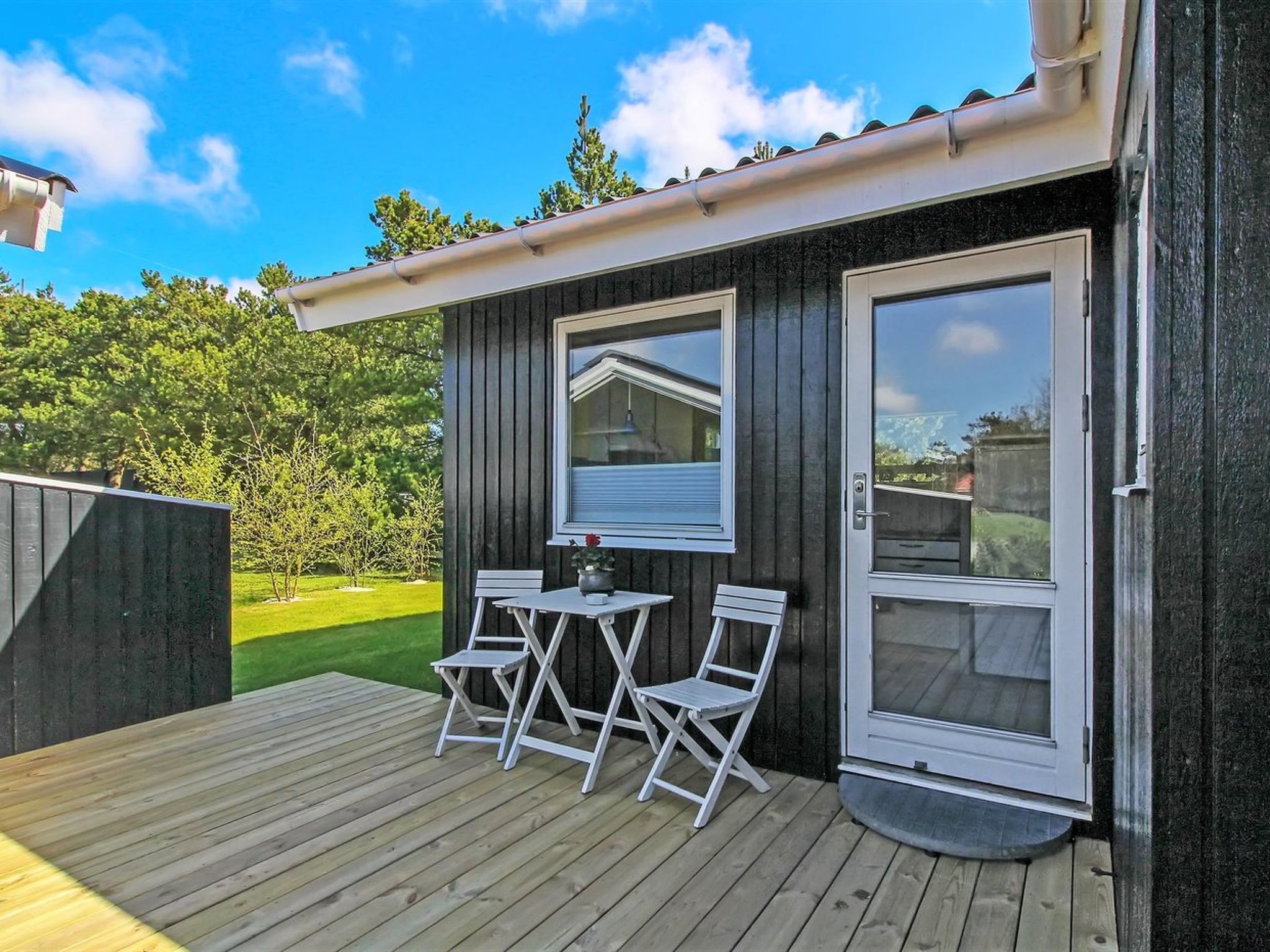 A wooden deck with a table and two chairs, a sliding glass door, and a view of a green landscape.