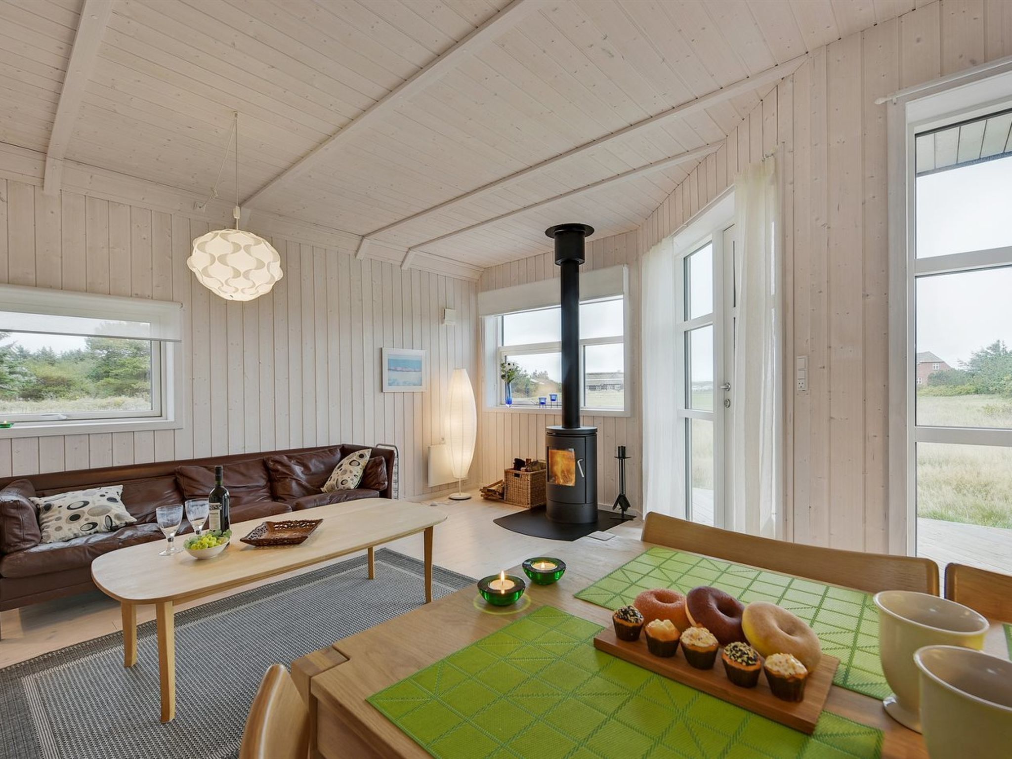 A cozy living room with a sofa, a table with snacks, a fireplace, and large windows.