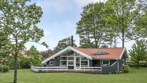 Ein modernes Haus mit einer großen Terrasse, umgeben von einer grünen Wiese und Bäumen.