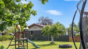 A backyard with a playset, a trampoline, and a house with a 'TUTTEN' sign.