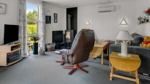 A modern living room with a large window, a fireplace, a leather chair, a TV, and a cozy sofa.