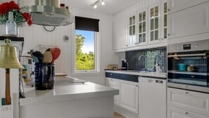 A modern kitchen with white cabinetry, a central island, a built-in oven, and a window with a view of greenery.