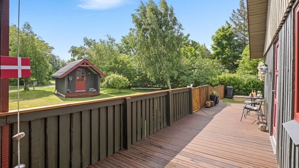 A wooden deck with a small shed, a flag, and a patio area with a table and chairs.