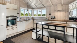 A modern kitchen with wooden paneling, a large island, and a view of greenery outside. - "Eljas" - 200m to the fjord by Interhome (Fur)