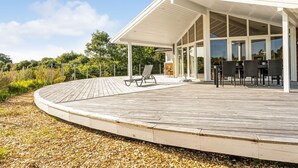 A modern outdoor patio with a wooden deck, a covered seating area, and a glass-enclosed space with tables and chairs. - "Eljas" - 200m to the fjord by Interhome (Fur)
