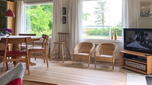 Een gezellige woonkamer met een houten vloer, een eettafel met stoelen, een televisie en rieten fauteuils.