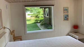 Een slaapkamer met een groot raam, een bed, een stoel, een nachtkastje en een lamp.