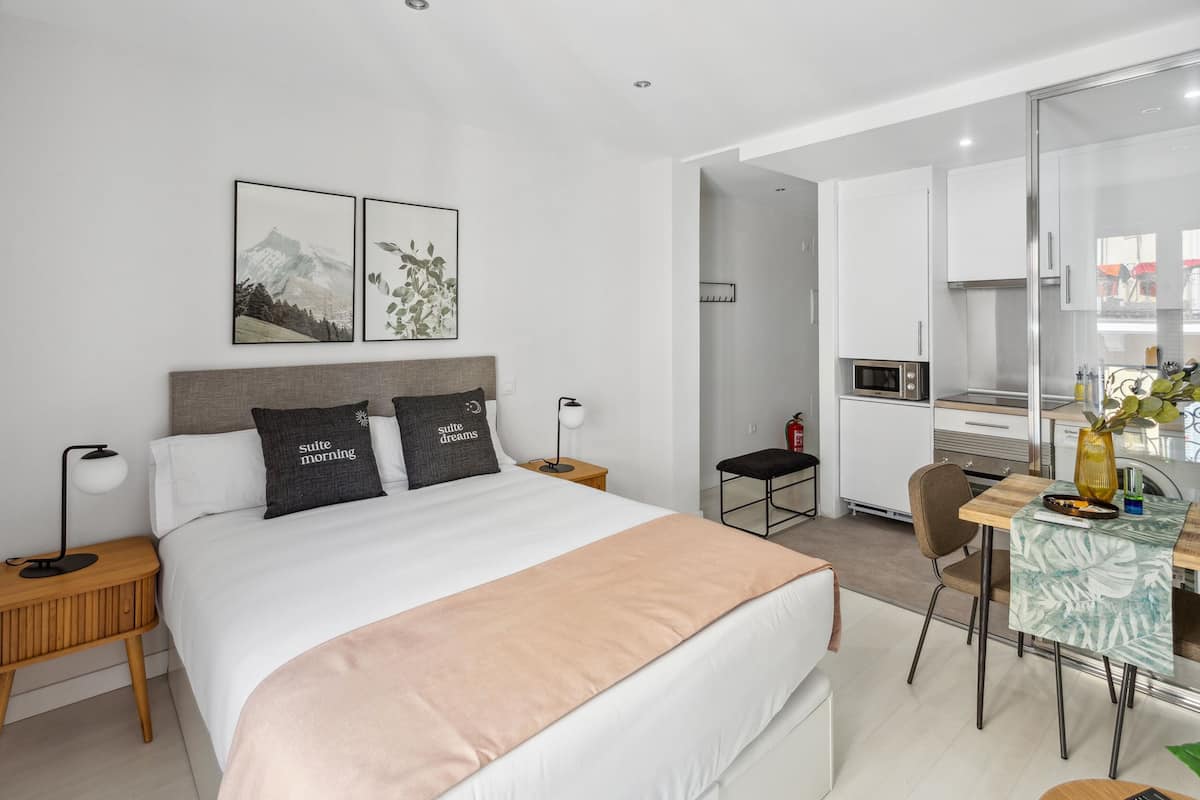 Una camera d'albergo moderna con un letto grande, una scrivania con una sedia, un forno a microonde e un angolo cottura.