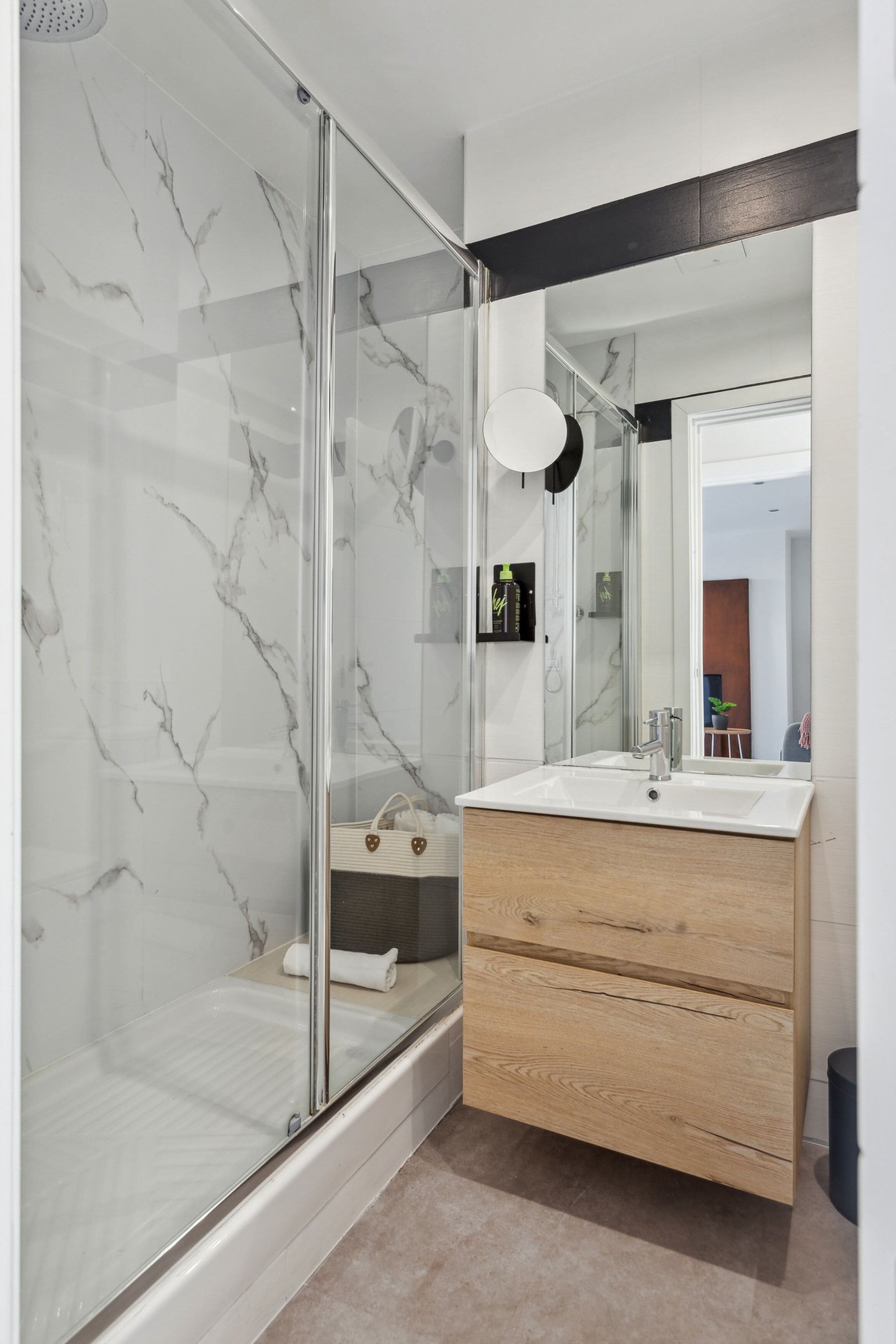 Een moderne badkamer met een glazen douchecabine, een houten wastafelmeubel en een grote spiegel.