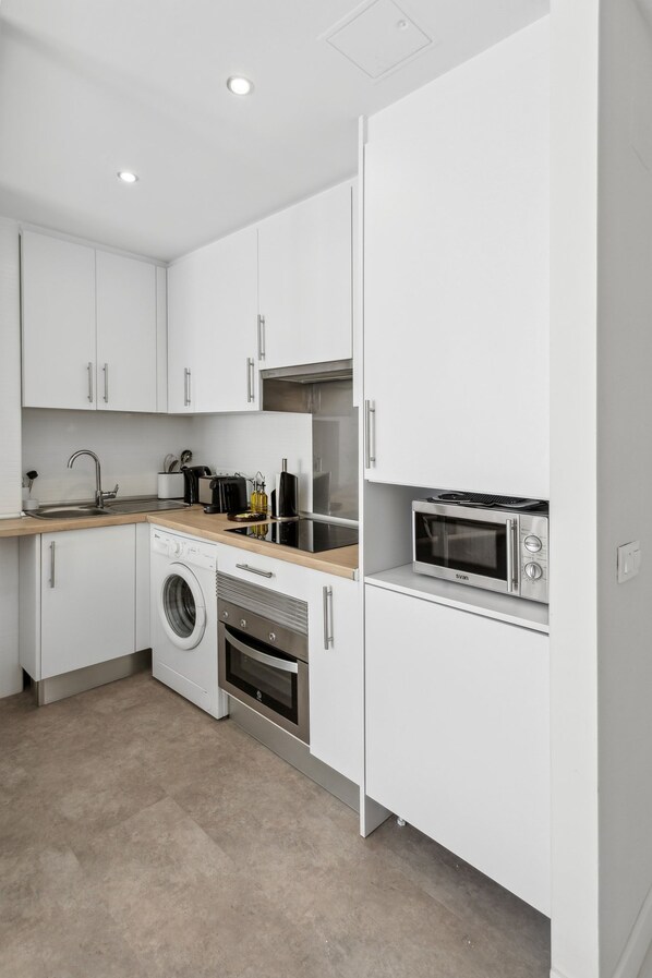 A modern kitchen with white cabinets, a washing machine, a microwave, and a sink.