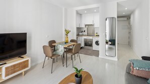 A modern living room with a flat-screen TV, dining area, kitchen, and a large mirror. - Limehome Madrid Calle de la Paloma (Madrid)