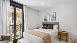 A modern bedroom with a bed, bedside tables, a remote control, a potted plant, and a balcony with a railing. - Limehome Madrid Calle de la Paloma (Madrid)
