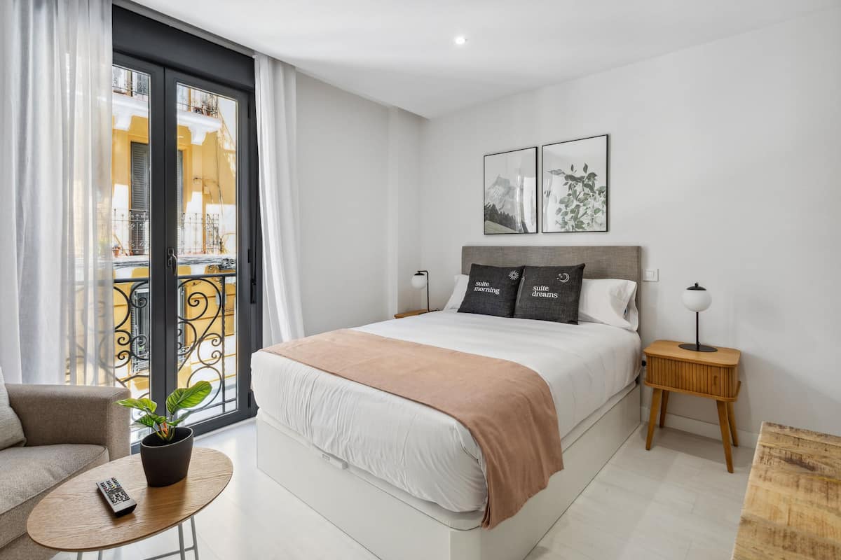 Camera da letto moderna con un letto, comodini, un telecomando, una pianta in vaso e un balcone con ringhiera.