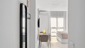 A modern hotel room with a minimalist design, featuring a large mirror, a dining area with a table and chairs, and a cozy seating area with a sofa and a lamp. - Limehome Madrid Calle de la Paloma (Madrid)
