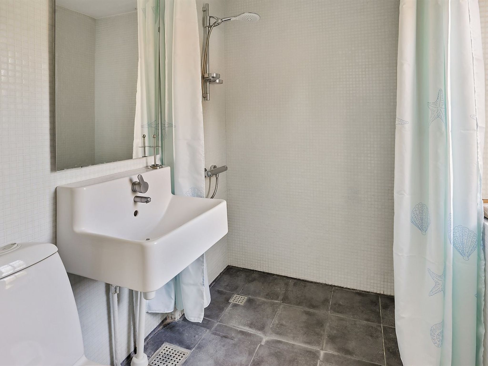 A bathroom with a white sink, a mirror, a shower with a glass door, and a tiled floor.