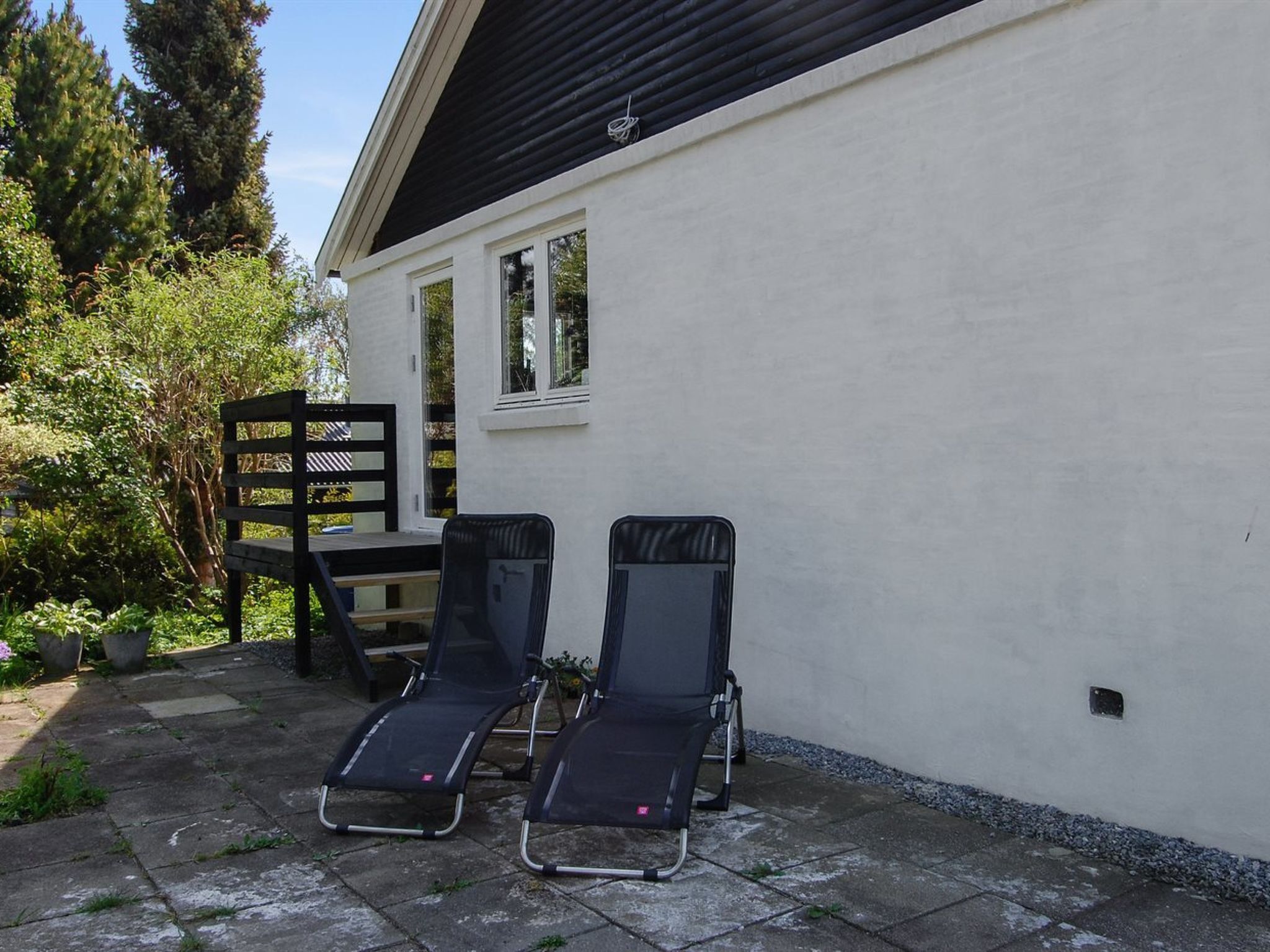 A patio with two lounge chairs, a wooden table, and a white building with windows.
