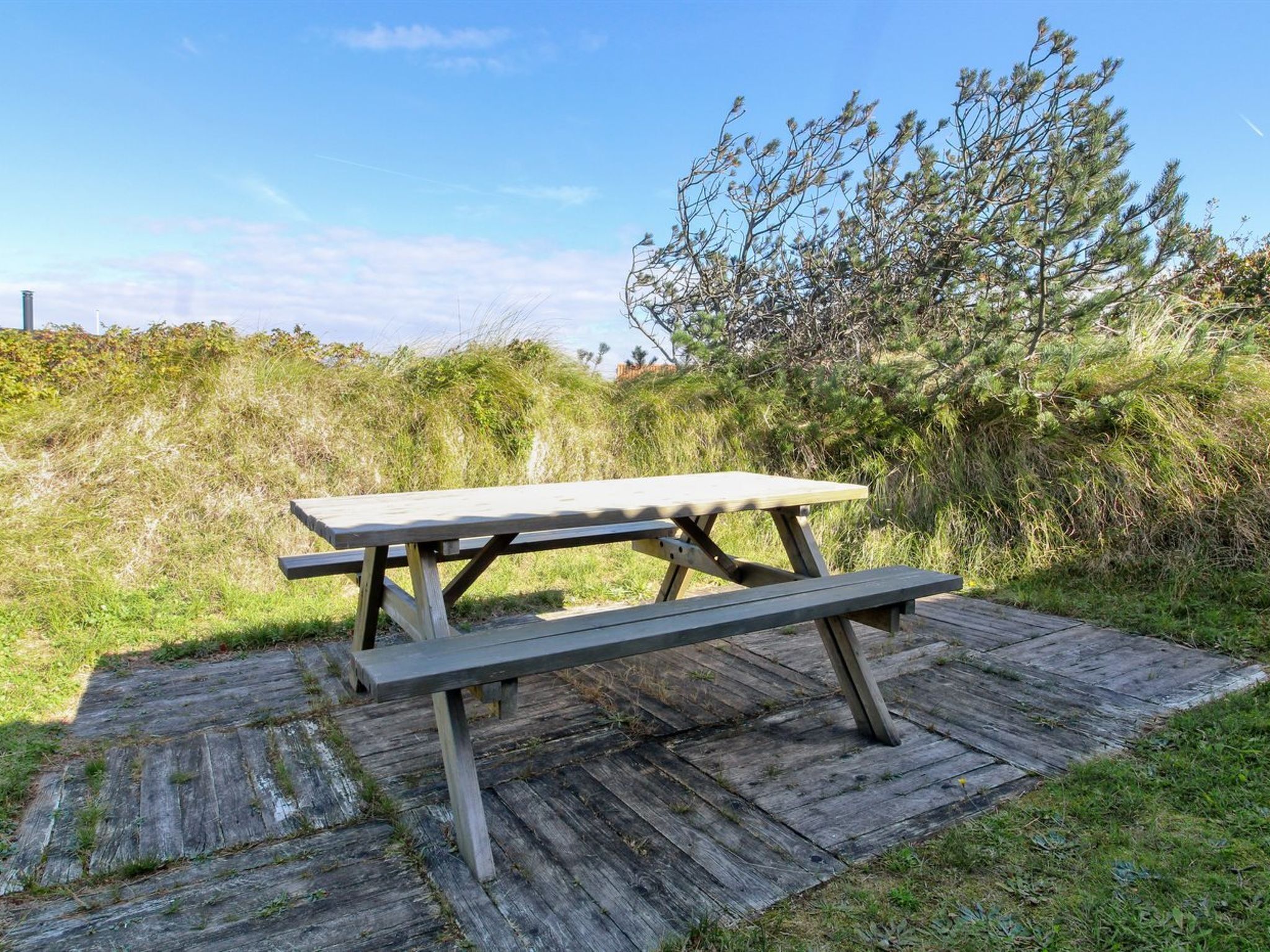 A picnic table on a wooden deck with a grassy and bushy background.