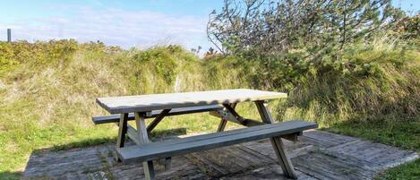 A picnic table on a wooden deck with a grassy and bushy background.