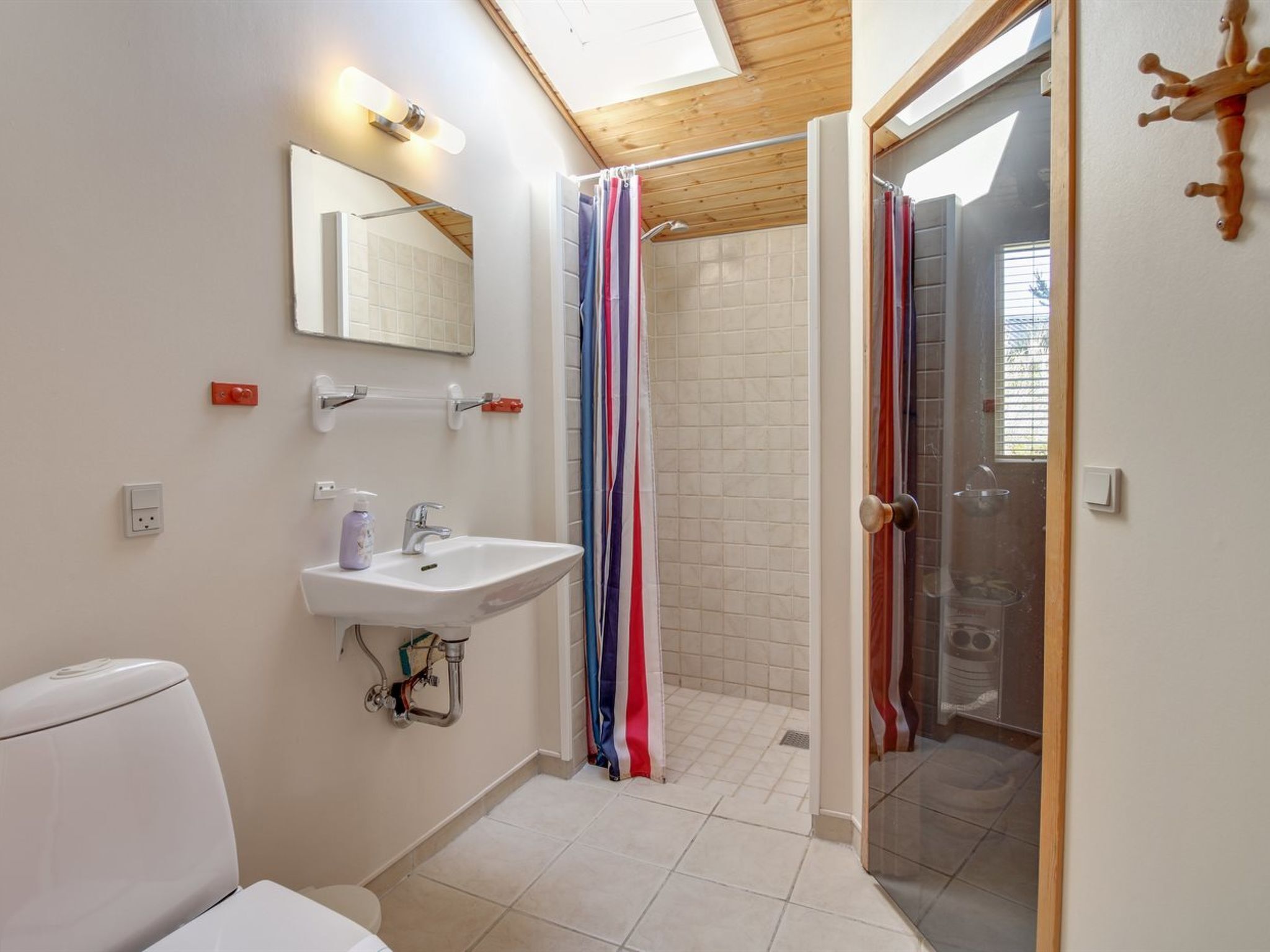 A modern bathroom with a skylight, a shower with a striped curtain, a white sink, and a toilet.
