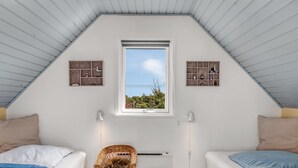 Une chambre avec deux lits, une chaise en osier, une petite table et une fenêtre donnant sur un beau paysage.
