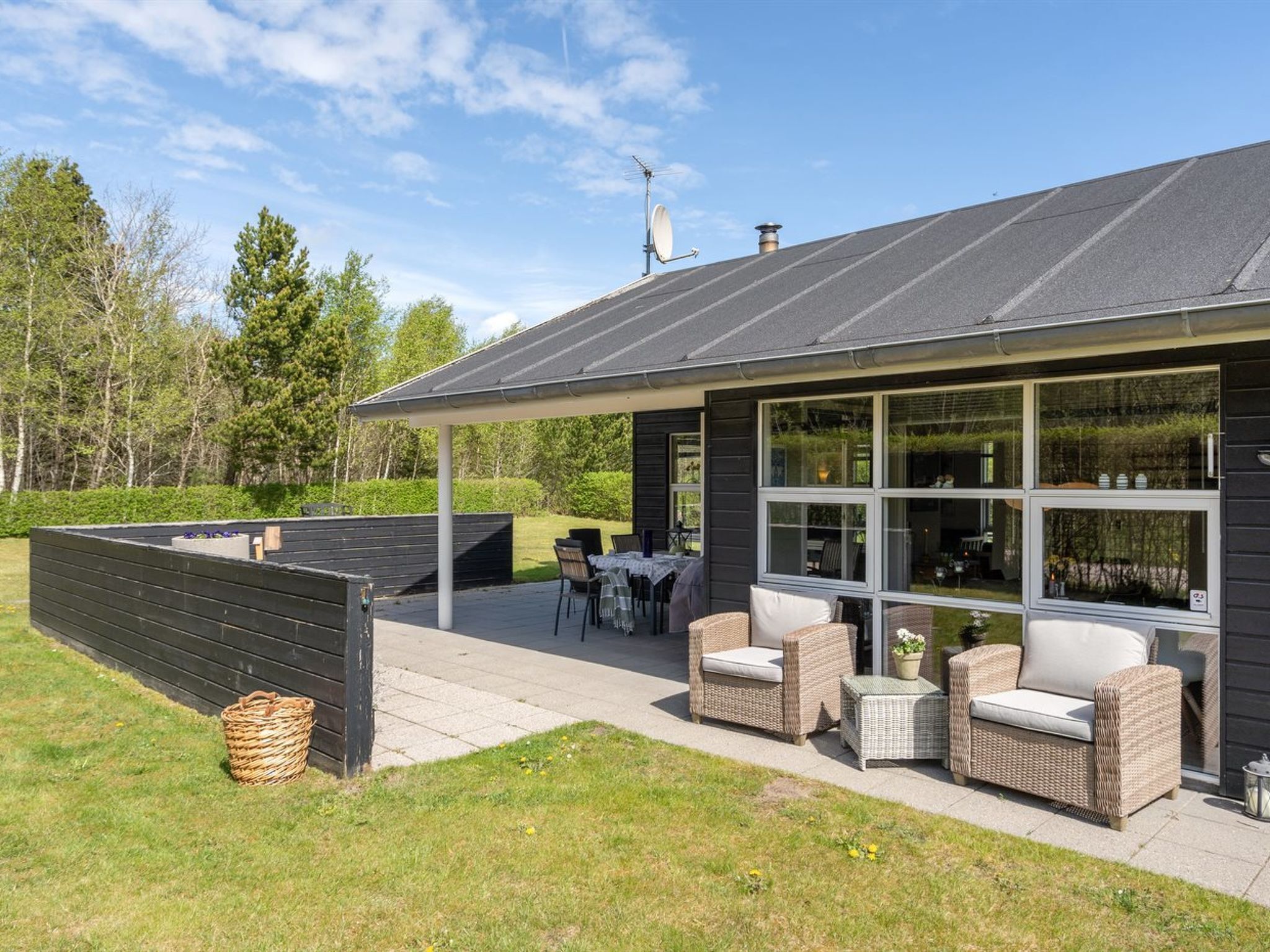 Et moderne hus med en overdækket terrasse, udendørs møbler og udsigt til den omkringliggende skov.