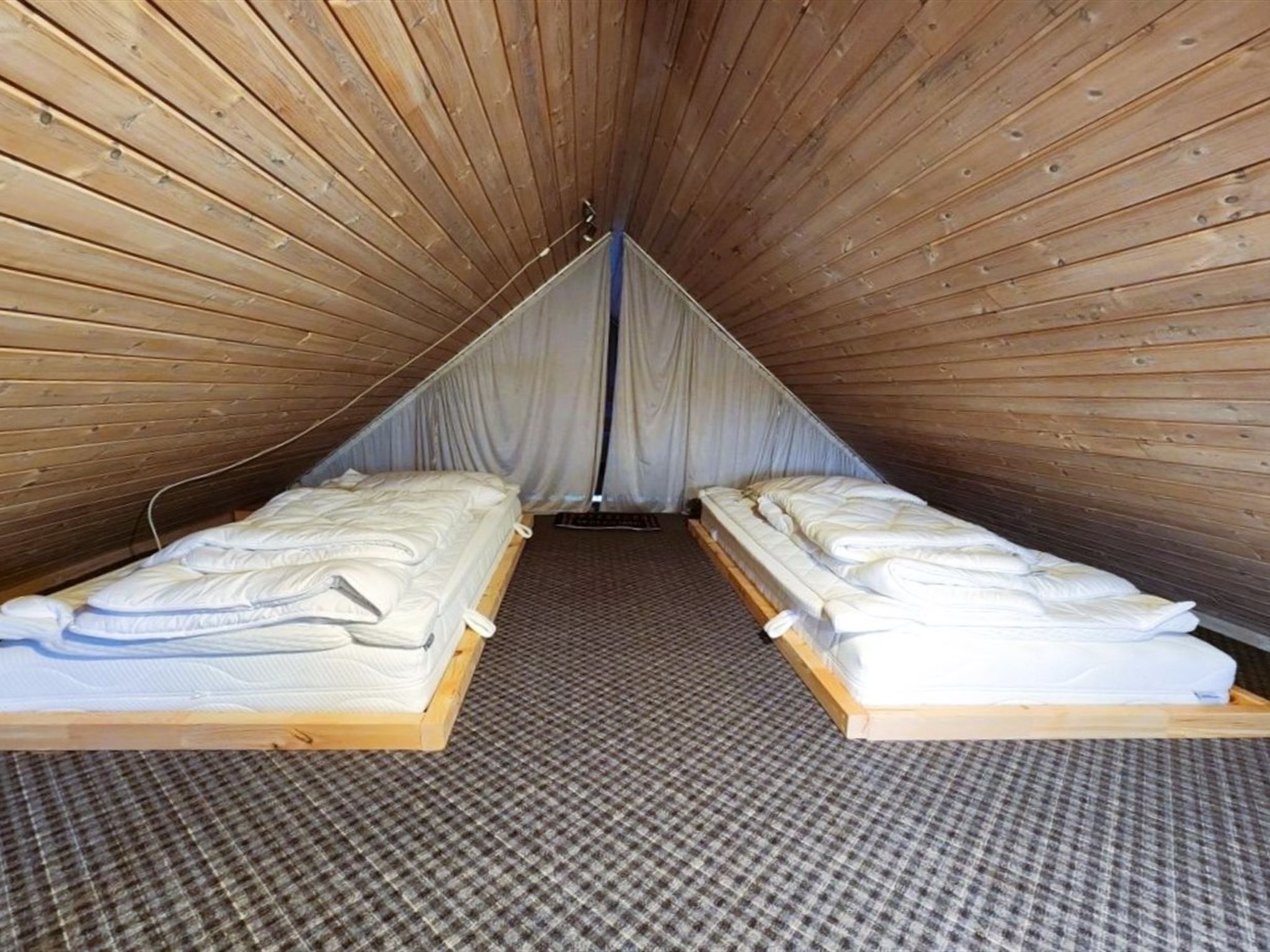 A small, triangular attic room with two beds and a checkered floor.