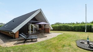 Une maison moderne avec un toit en pente, une terrasse dotée de mobilier d’extérieur et une pelouse bien entretenue.