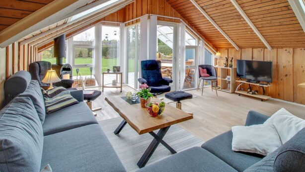 Ein geräumiges Loft mit hohen Decken, Holzbalken, einem großen Sofa, einem Fernseher und einem Essbereich mit Tisch und Stühlen.