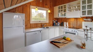 Eine Küche mit Holzwänden, einem Fenster, weißen Schränken und einer Arbeitsplatte mit Schneidebrett und Messer.