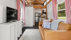 A compact living space with a kitchenette, a television, a sofa with cushions, and a ceiling fan.