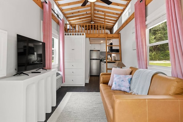A compact living space with a kitchenette, a television, a sofa with cushions, and a ceiling fan.