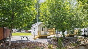 A small cabin with a deck, a picnic table, and a stream.
