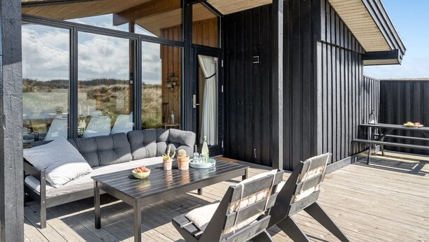 Un área de estar exterior moderna con terraza de madera, un sofá y una mesa decorada para exteriores.