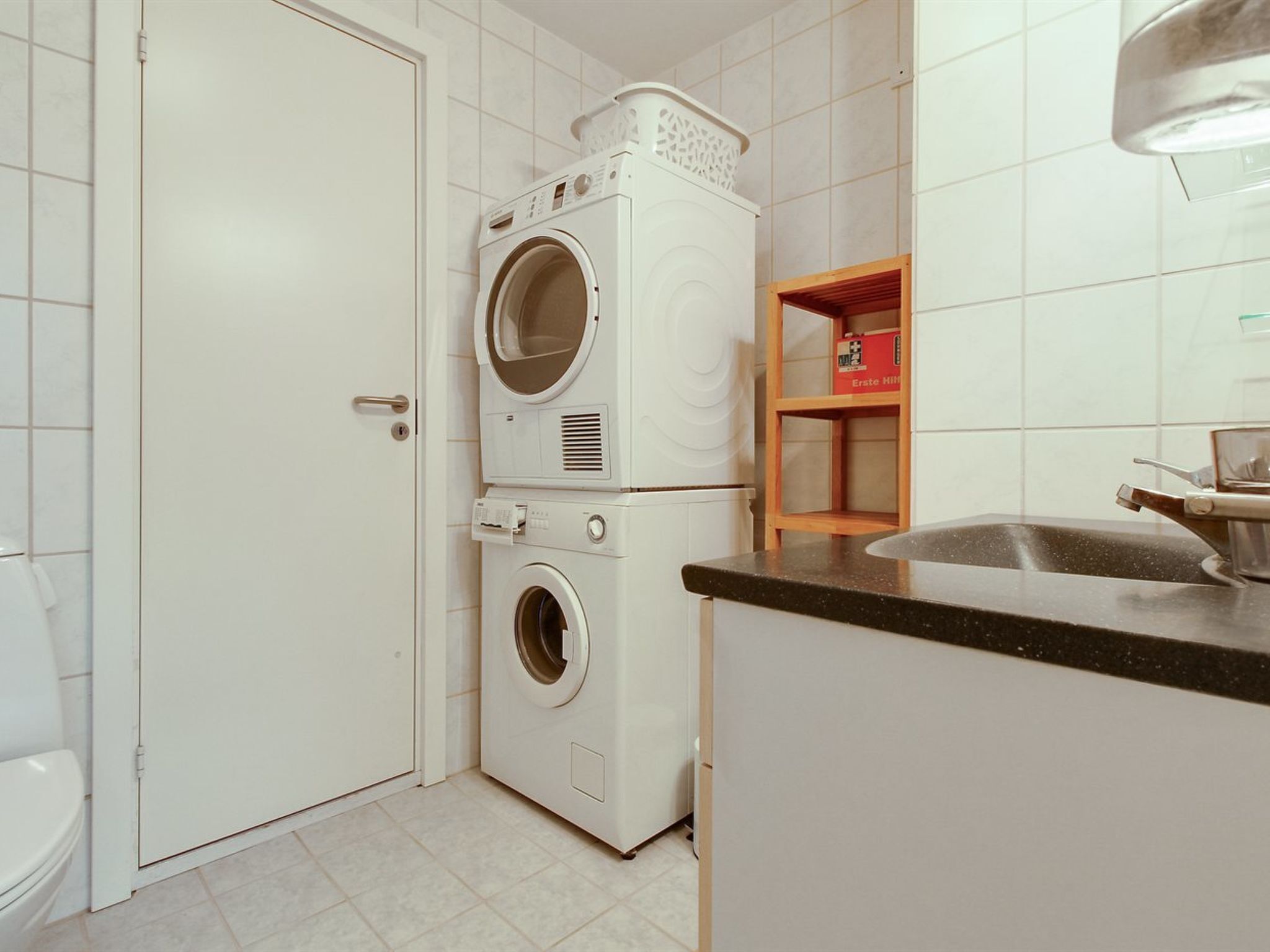 Un espace buanderie compact comprenant un lave-linge, un sèche-linge et un panier à linge empilable.