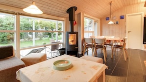 Una habitación acogedora con chimenea, techo de madera y ventanas amplias con vistas a un jardín.