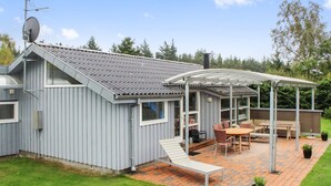 Una casa moderna con un patio que incluye una mesa y sillas, un espacio de estar cubierto y una antena parabólica.