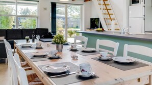 A modern dining area with a long table set for a meal, a kitchen area with a microwave and refrigerator, and a staircase leading to an upper level. - "Ilkka" - 175m from the sea by Interhome (Rødvig Stevns)