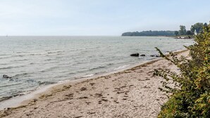 A beach with calm waters, a sandy shore, and a distant shoreline with trees and a structure. - "Ilkka" - 175m from the sea by Interhome (Rødvig Stevns)