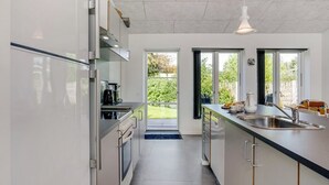 A modern kitchen with a large island, stainless steel appliances, and a view of the garden through the sliding doors. - "Ilkka" - 175m from the sea by Interhome (Rødvig Stevns)