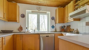 A kitchen with wooden cabinets, a stainless steel dishwasher, a window with a view of trees, and a clock on the wall. - "Eina" - 250m from the sea by Interhome (Hals)