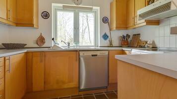 Une cuisine avec des armoires en bois, un lave-vaisselle en acier inoxydable, une fenêtre donnant sur les arbres et une horloge au mur.