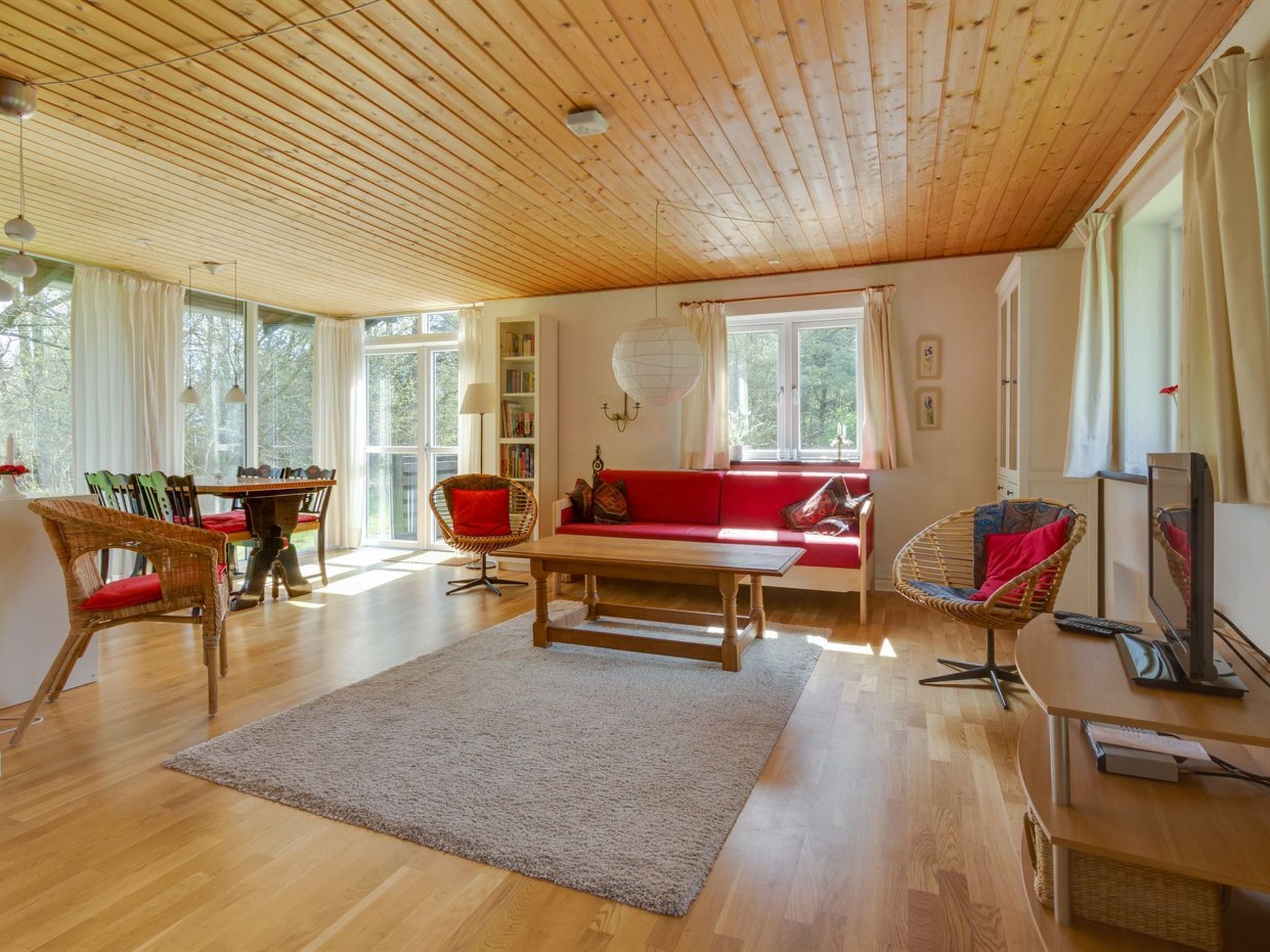 Un salon spacieux avec un plafond en bois, un canapé rouge, une table à manger avec des chaises et un téléviseur.