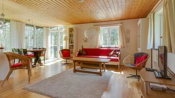 Un salon spacieux avec un plafond en bois, un canapé rouge, une table à manger avec des chaises et un téléviseur.