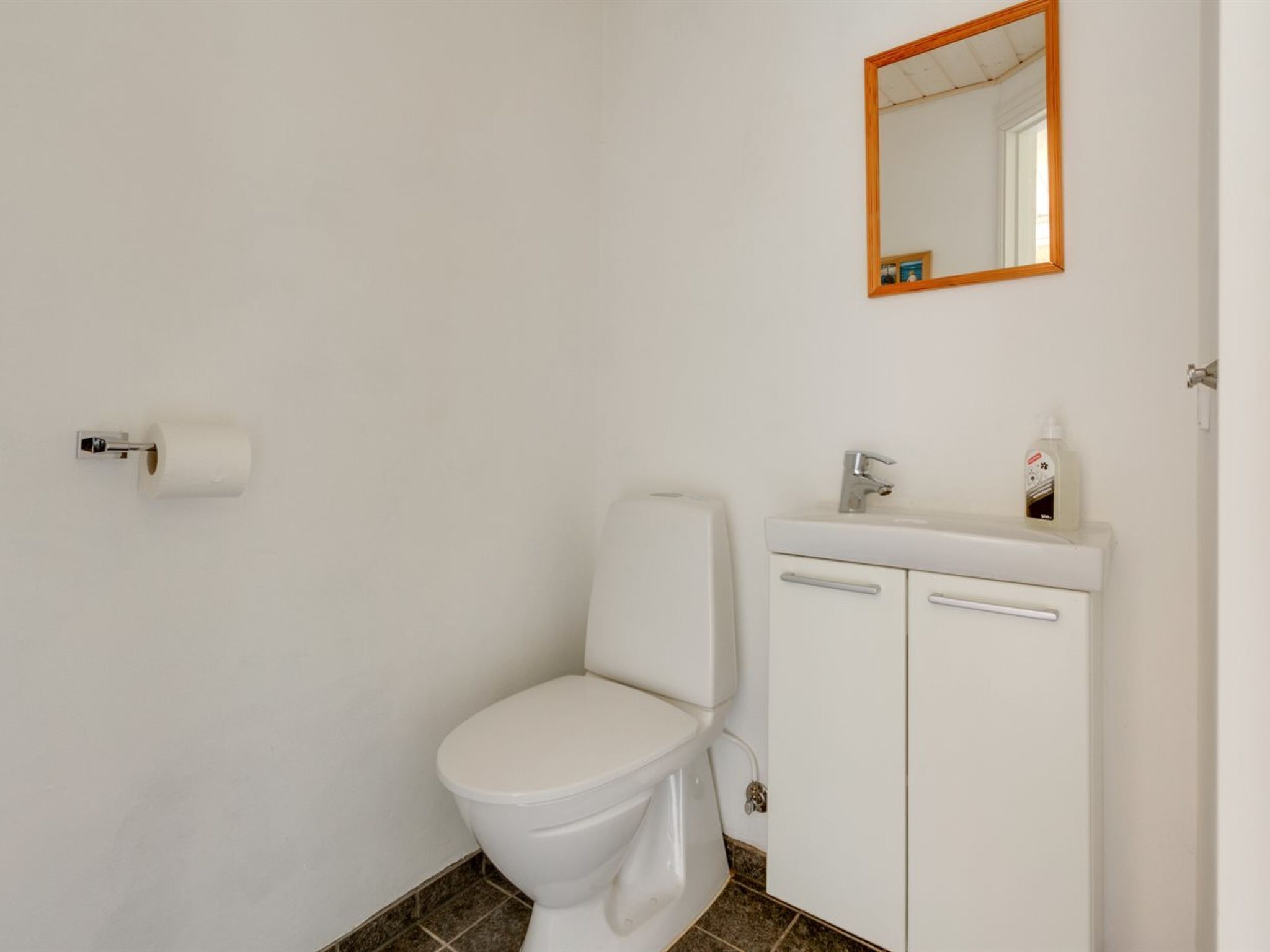 A bathroom with a toilet, a sink, a mirror, and a roll of toilet paper.