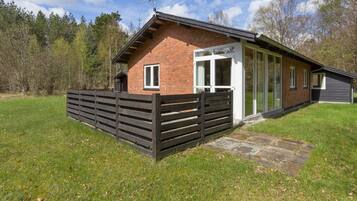 Une maison de plain-pied en briques, avec une clôture en bois, une porte en verre et une antenne parabolique.
