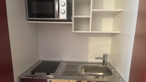 A compact kitchenette with a microwave, stove, sink, and storage cabinets. - Furnished apartment for 1 person (Büchlberg)