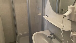 A bathroom with a shower, sink, and a hairdryer on the wall. - Furnished apartment for 1 person (Büchlberg)