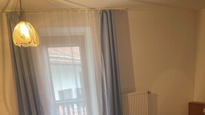 A bedroom with a bed, a chair, a radiator, and a window with curtains. - Furnished apartment for 1 person (Büchlberg)